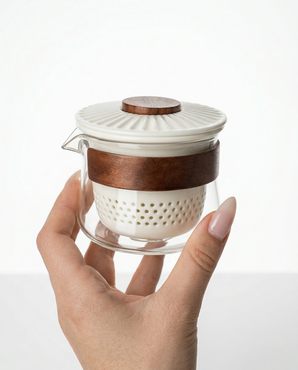 Hand holding a small glass infuser for gongfu ceremony with wooden accents on a white background