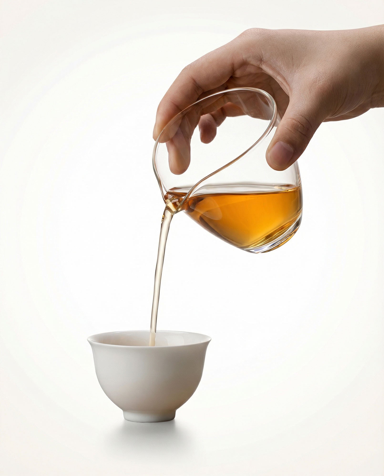 Hand pouring tea from a fair cut teapot into a white cup during gonfu ceremony in Dubai