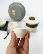 Person holding a small white ceramic cup with more cups and a gray case in the background.