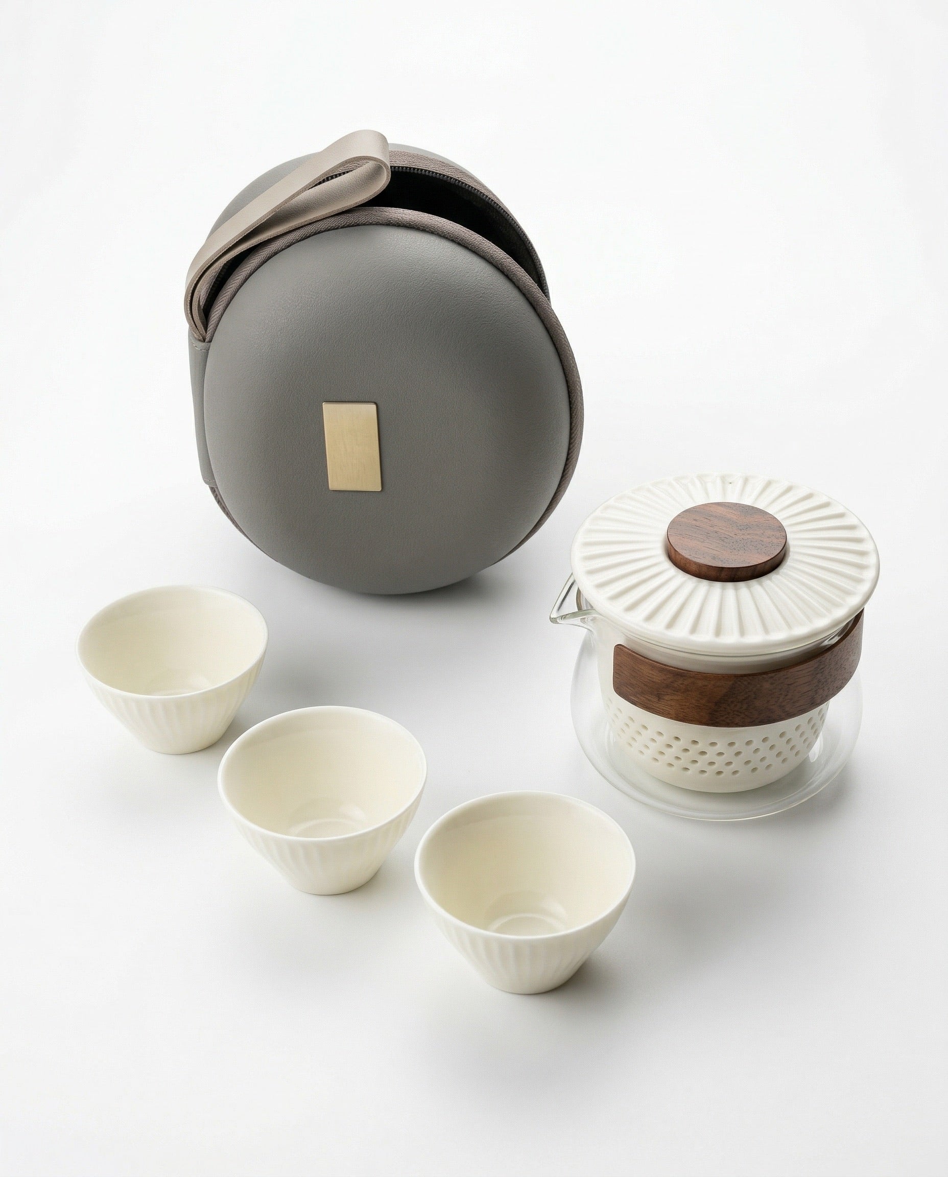 Travel compact tea set with ceramic cups, glass teapot, and round gray carrying case on a white background